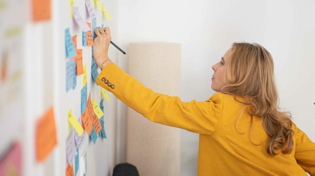 Josefine Schulze beugt sich nach vorne, um etwas auf ein Post-it an einer Wand voller Notizen zu schreiben.