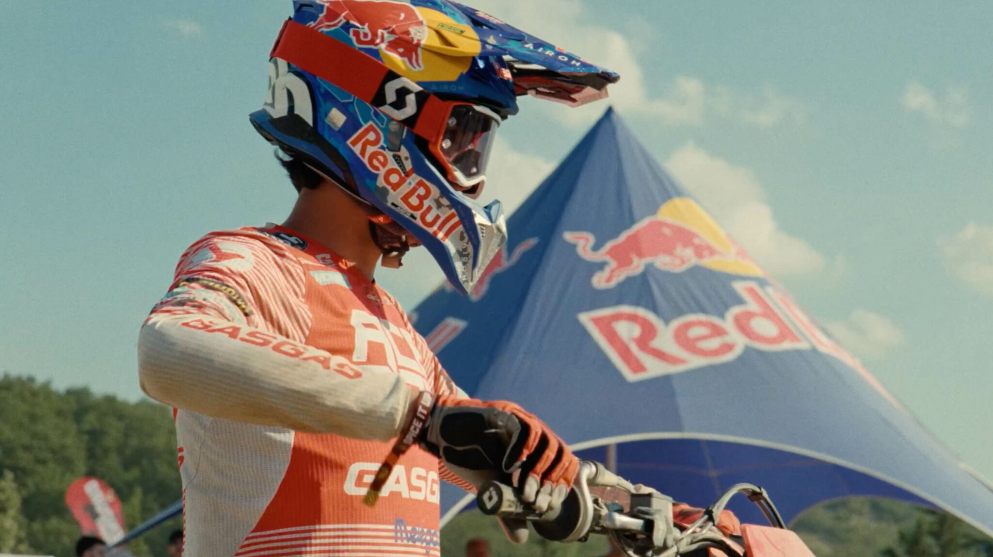 Nahaufnahme eines Motocross-Fahrers mit Helm, im Hintergrund unscharf ein Red Bull Zelt.