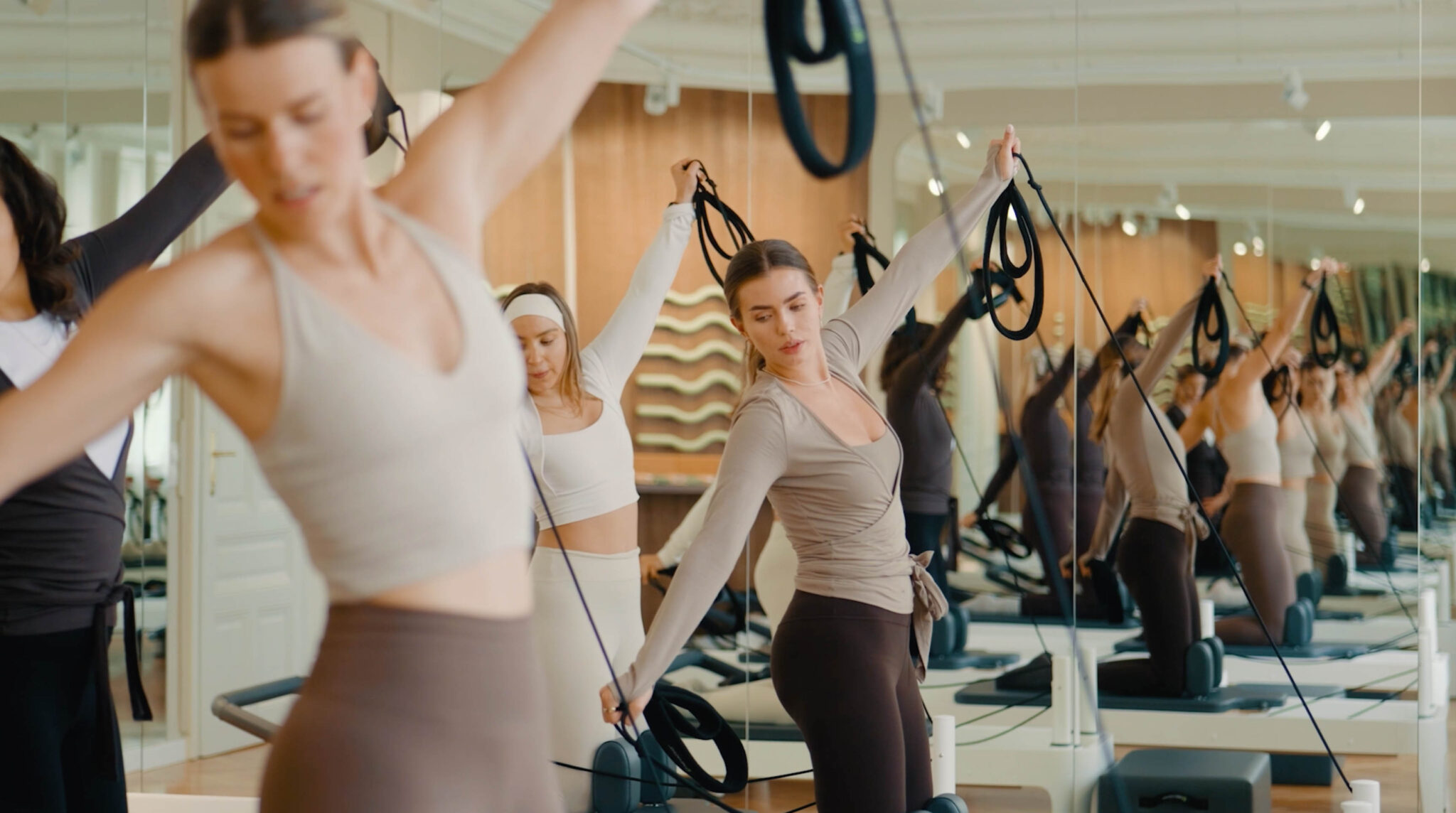 Frauen trainieren gemeinsam auf Reformer-Pilates-Geräten in einem hellen, modernen Studio. Die Szene zeigt Konzentration, Bewegung und eine ruhige, fokussierte Atmosphäre.